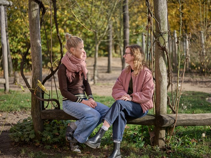 Zwei Frauen sitzen im Herbst auf einer rustikalen Holzbank im Freien und führen ein vertrauensvolles Gespräch – ein Bild für den persönlichen Austausch in der Waldorfpädagogik.